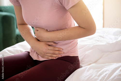 Woman suffering from stomachache is sitting on the bed and clutching her stomach 