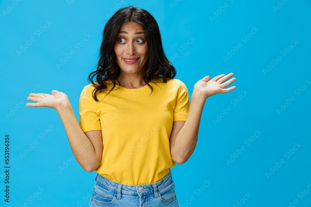 Woman in yellow t-shirt on blue background posing gestures emotions and signals with smile, hands up happiness copy space