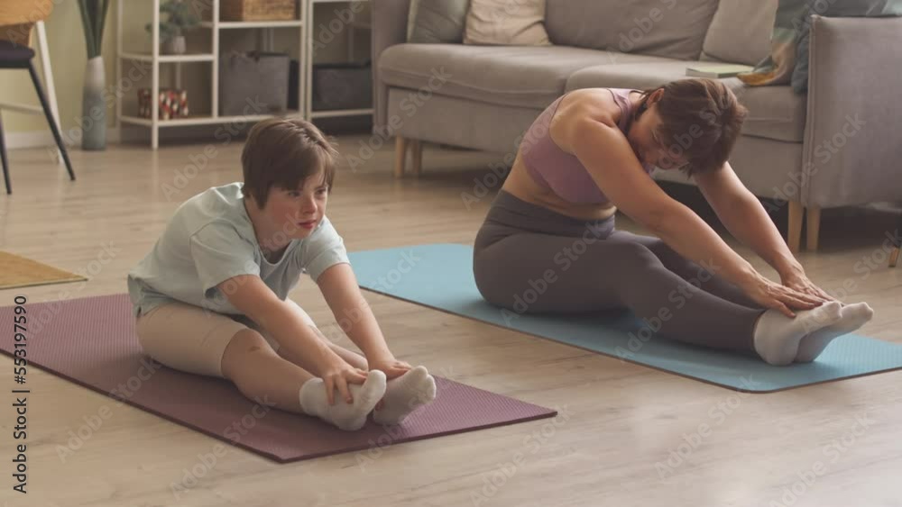 14 year old Caucasian girl with down syndrome and her mother stretching on mats while exercising at home