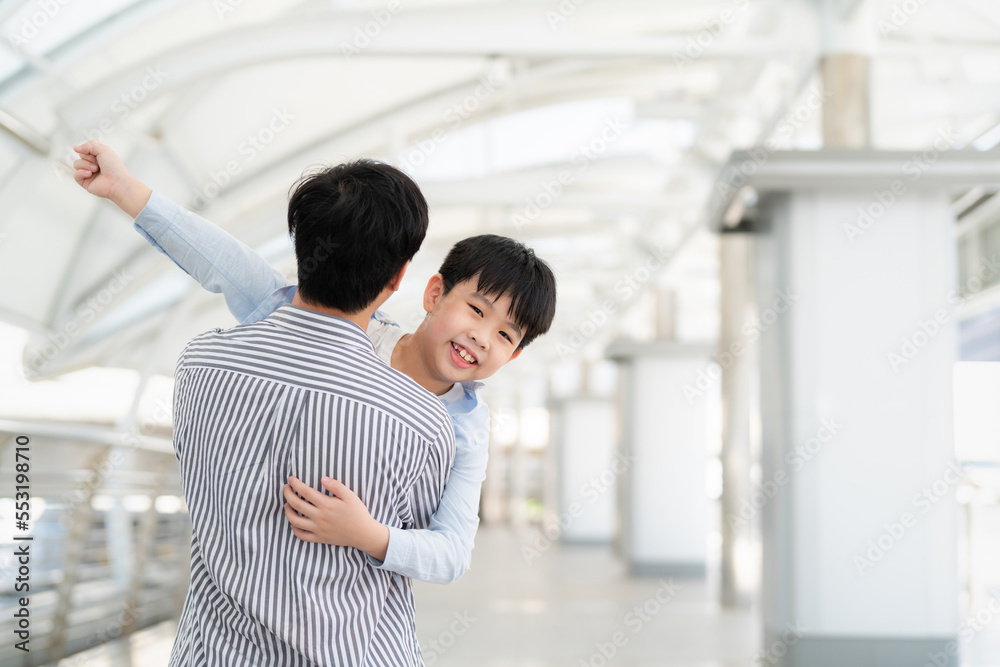 Asia little boy hug his father at the airport sky walk and raise hand up with smile on sunny day. Happy for traveling trip during vacation. Family relation father and son. Tourist at the central city