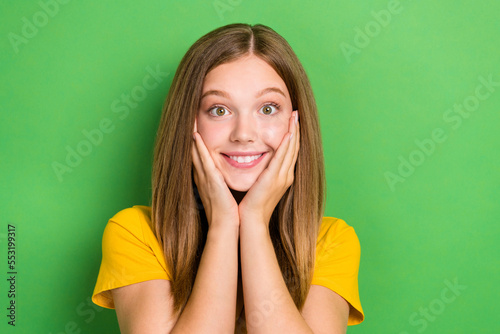 Closeup portrait of funny toothy beaming smile brown hair schoolgirl teenager touch cheeks excited good mood isolated on green color background