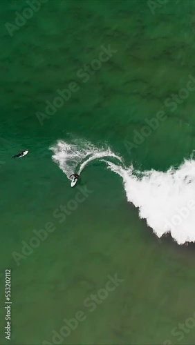 surfer riding a wave on a crystal clear water beach, aerial view from drone, vertical video for smart phone
