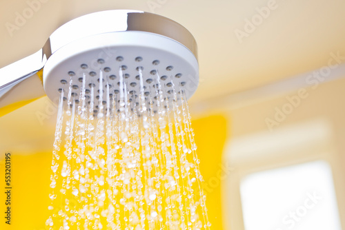 Close-up of flowing water drops from a shower head in a bright bathroom