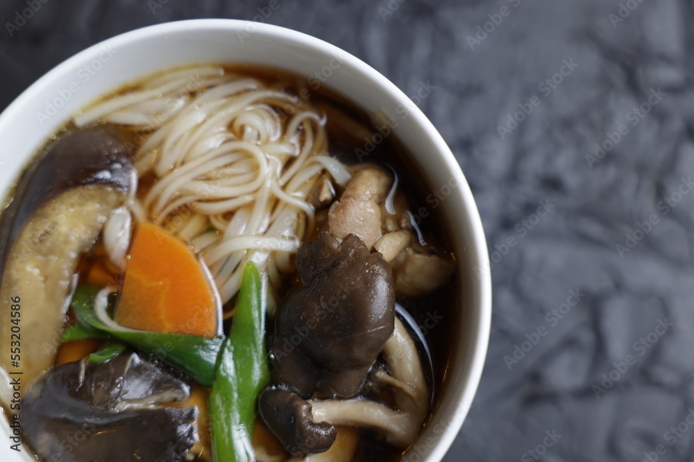 Mushroom soup udon noodles with fresh green onions in a fine white bowl against a black design board, a traditional Japanese meal. Mushroom soup udon noodles with fresh green onions in a fine white bowl against a black design board, a traditional Japanese meal.