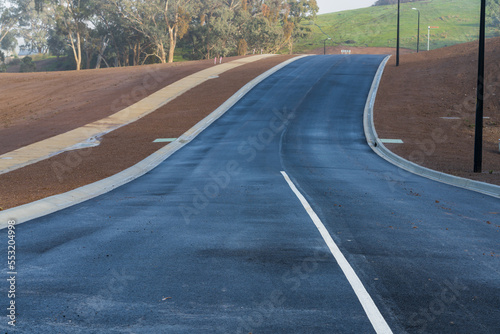 A newly laid bitumen road leading over a rise through a new residential development