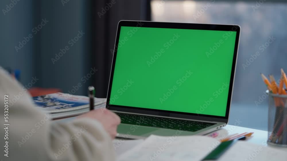 Woman Uses Laptop with Green Mock-up Screen. Girl Student Taking Notes on Notebook from Laptop at Online Lesson