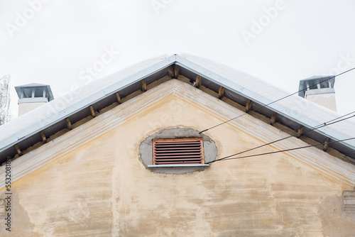 Two smoke, rectangular, exhaust pipes on the roof of an old house. The roof of the building is covered with white snow against the gray sky. Cloudy, cold winter day, soft light.