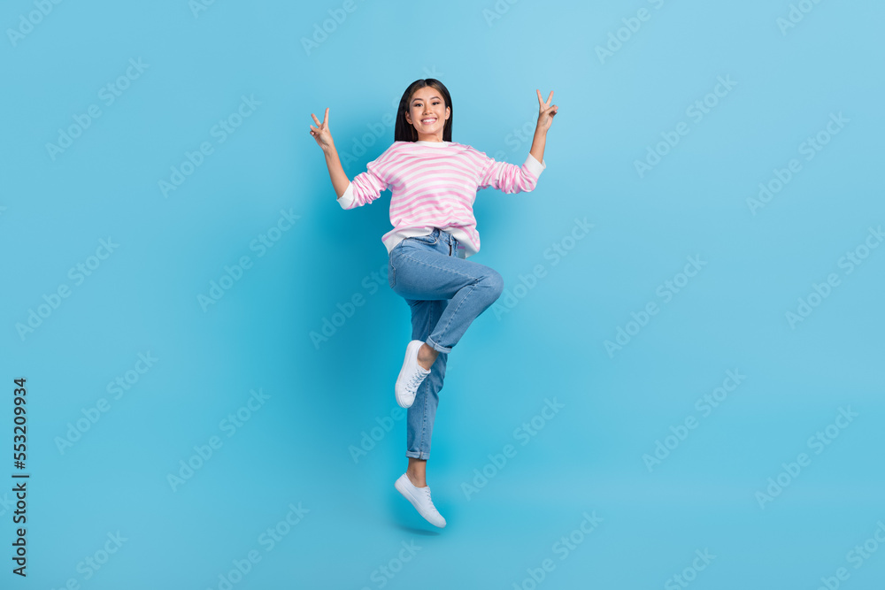 Full length photo of cute pretty lady wear striped sweater jumping high showing v-signs isolated blue color background