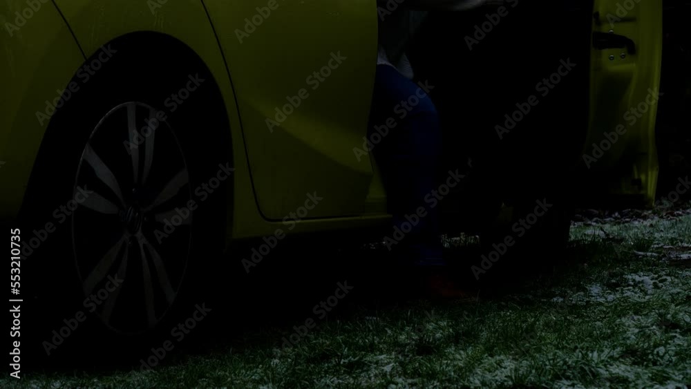 Closeup outside in early morning or night darkness, with frost on the grass, an adult person, opening a car door, then slowly and carefully getting out, then shutting the door and walking away,