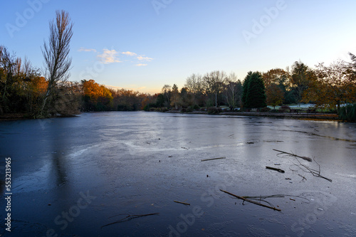 A frozen lake at sunset. There is ice on the surface of the lake in this winter scene. A cold winter's day in Kelsey Park, Beckenham, Kent, UK. photo