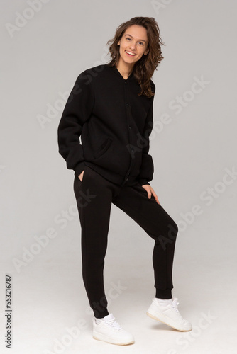 Obraz na płótnie Smiling woman with thick curly hair in a black suit of hoodies and sweatpants. Mock-up. w salonie