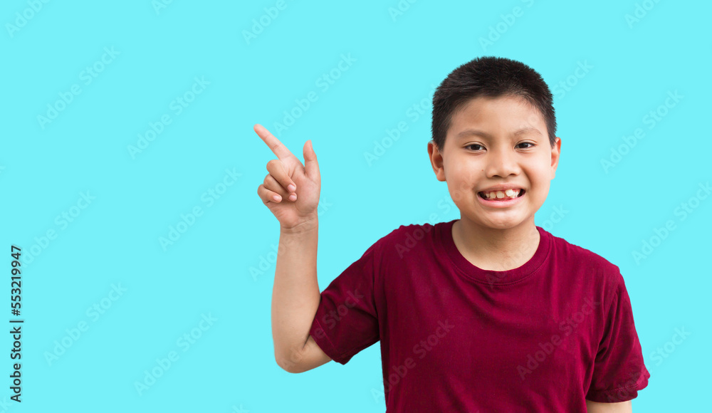 Smiling happy Asian boy pointing his finger away at copy space isolated over a plain blue background Smiling happy Asian boy pointing his finger away at copy space isolated over a plain blue background