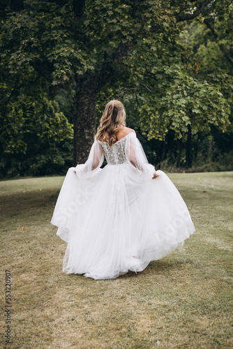 Wedding. A bride in a white dress walks along the green grass against the background of trees © AlexGukalovUkraine