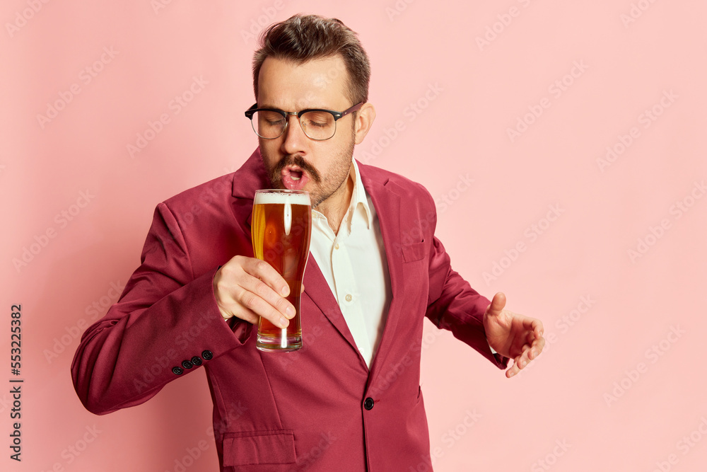 Portrait of stylish emotive businessman in a suit posing with lager beer mug isolated on pink background. First sip Portrait of stylish emotive businessman in a suit posing with lager beer mug isolated on pink background. First sip