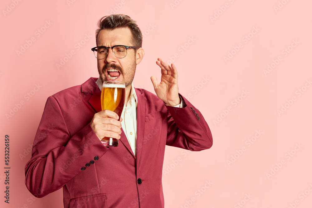 Portrait of stylish emotive man in a suit posing with glass of lager beer isolated on pink background. Hangover party Portrait of stylish emotive man in a suit posing with glass of lager beer isolated on pink background. Hangover party