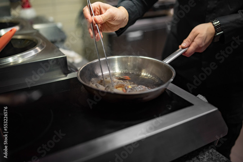 man chef cooking tasty shrimp in frying pan on kitchen