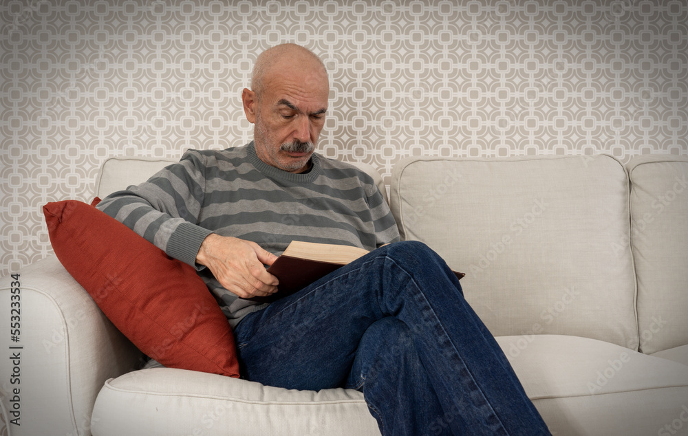 Happy Senior Man Sitting on Sofa and Reading Book at Home