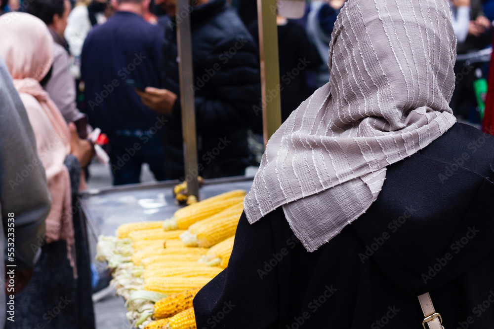 Anonymous muslim women with hijab buying corn on the cob at market stall on crowded street in Istanbul, Turkey