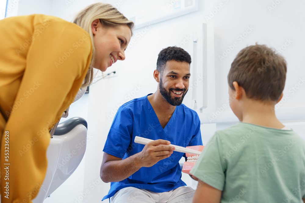 Obraz premium Young multiracial dentist showing little boy how to clean teeth, concept of children oral hygiene,prevention and dental health.