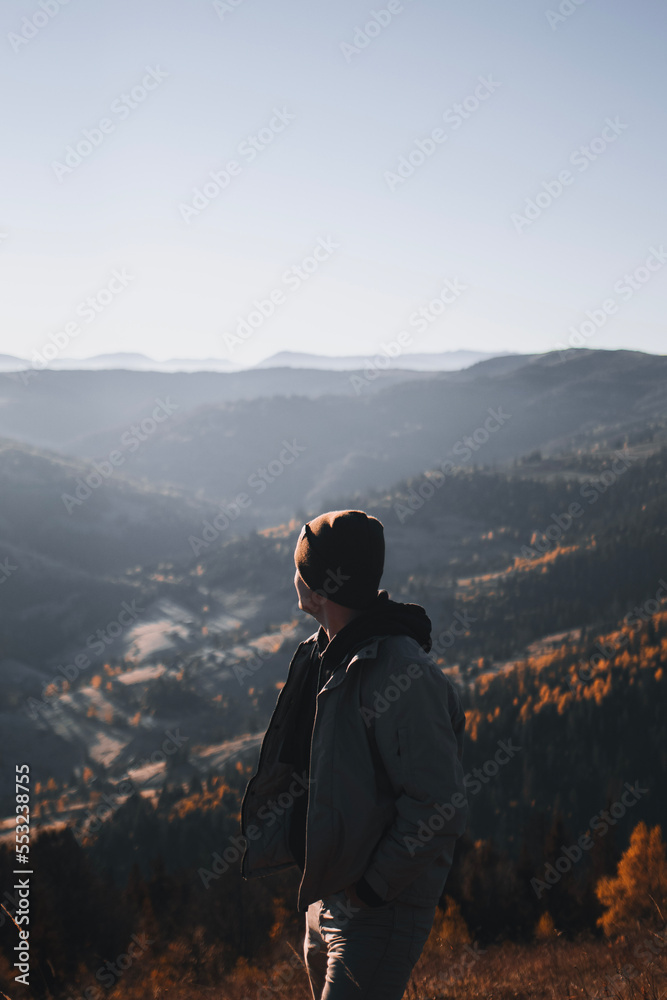 Young man is standing and looking away at the mountains autumn landscape