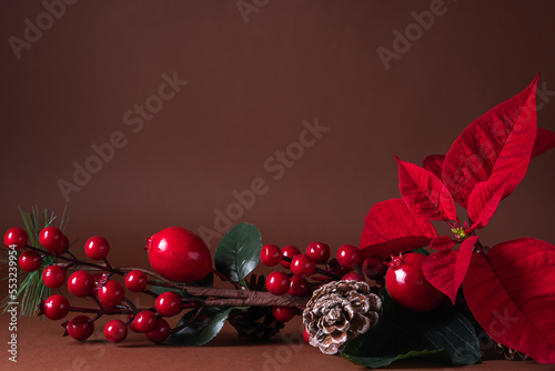 Holiday card - red flower poinsettia, fir cone, Christmas decorations on brown background. Flat lay, top view.