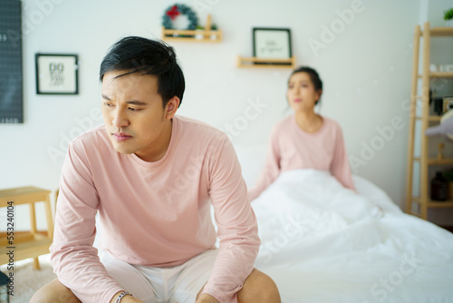 Unhappy - stressful Asian man sitting on the bed while his wife shouting at him. Critical or serious arguing between husband and wife about a problem in family.