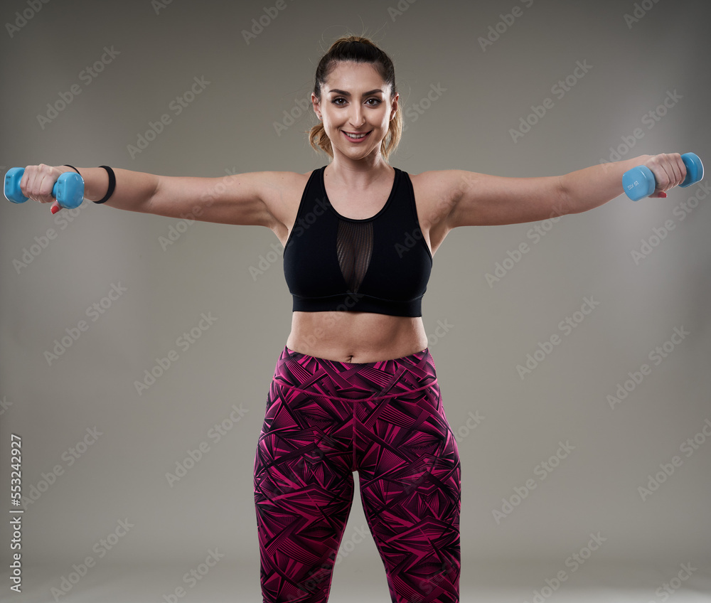 Plus size woman working out with dumbbells on gray Plus size woman working out with dumbbells on gray