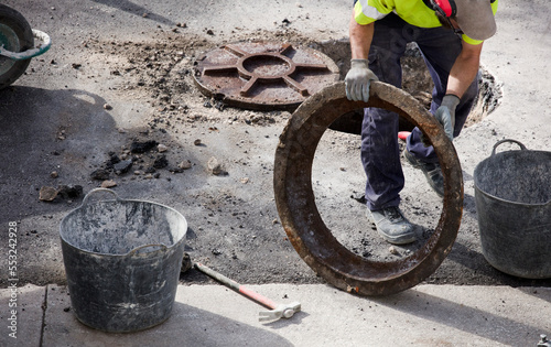 sewage and manhole in hands of worker in uniform and asphalt at construction site
