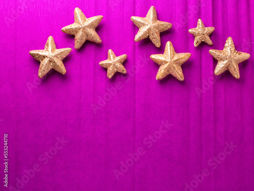 Border with big and small golden decorative stars on bright pink paper textured background. Top view. Christmas, New Year holidays concept. Place for text.