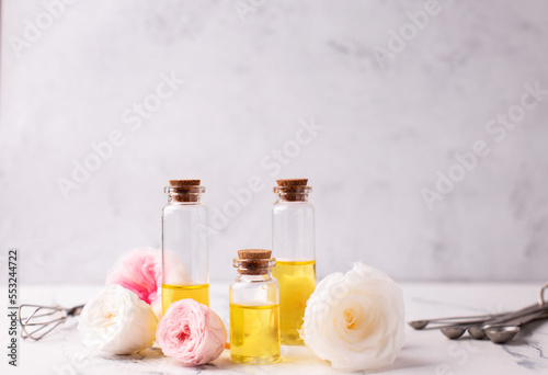 Three bottles with rose essential aroma oil and rose flowers on light  grey textured background. Selective focus is on left bottle. Place for text..