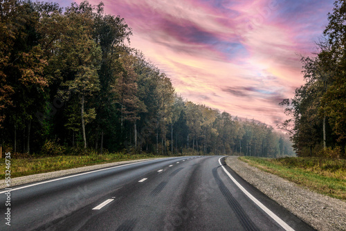 A winding road in the forest, with a colorful sky. Traces of braking on the asphalt
