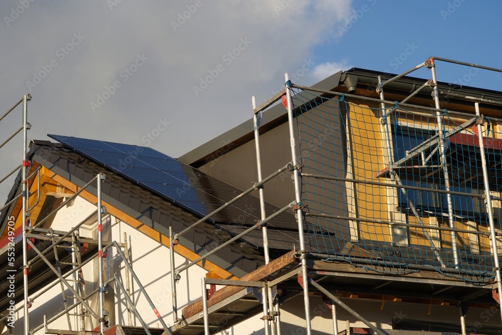 Residential house roof with scaffolding in the expansion phase. Solar modules have already been mounted on the roof