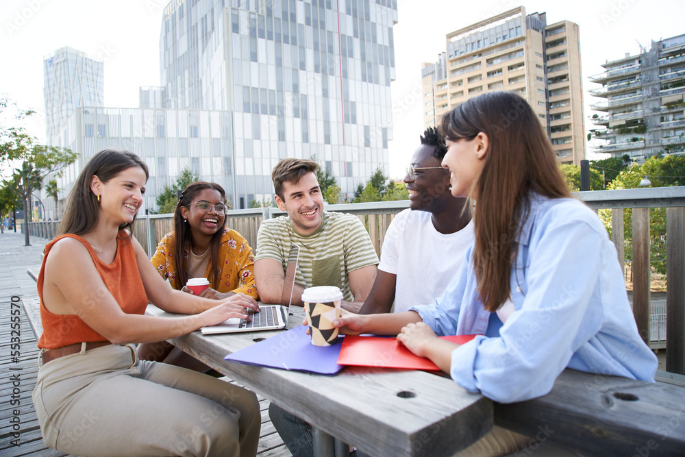 Group of cheerful students studying together outdoors. College classmates review for exam together sitting on a bench on campus. Group of cheerful students studying together outdoors. College classmates review for exam together sitting on a bench on campus.