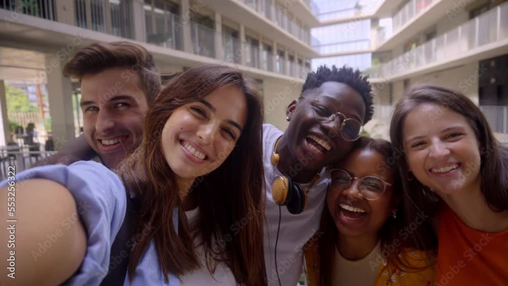 Group of multinational student friends taking a selfie while being at university, looking at camera smiling. Erasmus colleagues using social media to do streaming.