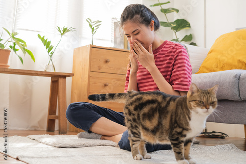 Obraz na plátně Asian young woman, girl hand in sneezing from fur allergy while playing with her lovely cat, pet on carpet in living room at home, apartment