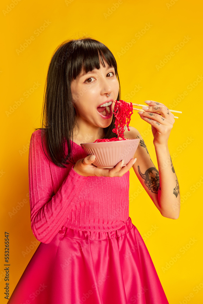 One young beautiful girl in bright pink dress posing with pink noodles isolated on vivid yellow background. Concept of youth, beauty, fashion, lifestyle, emotions One young beautiful girl in bright pink dress posing with pink noodles isolated on vivid yellow background. Concept of youth, beauty, fashion, lifestyle, emotions