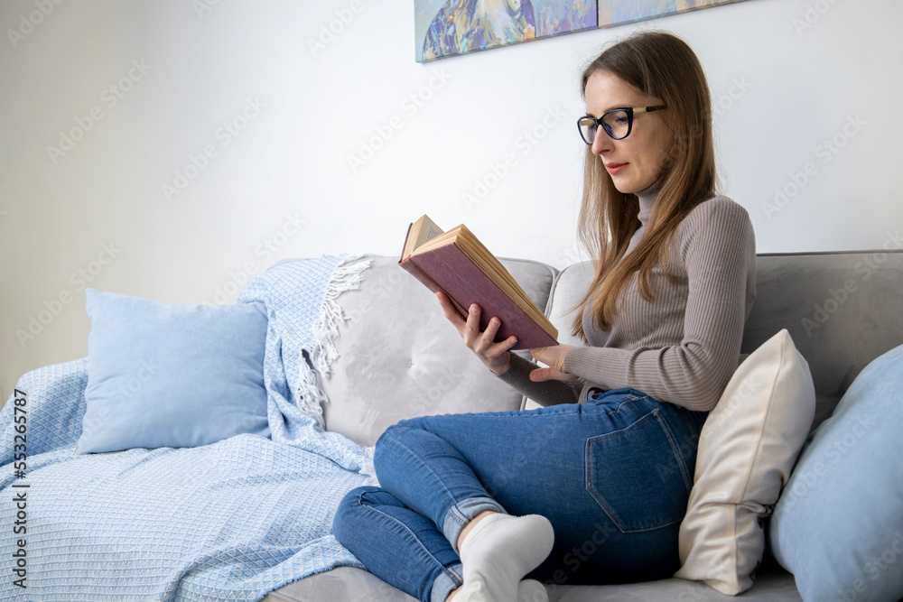 Young woman in glasses sitting on a sofa reading a book Young woman in glasses sitting on a sofa reading a book