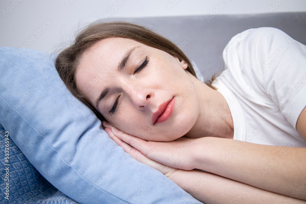 Sleeping young woman in white t-shirt lying on gray sofa Sleeping young woman in white t-shirt lying on gray sofa