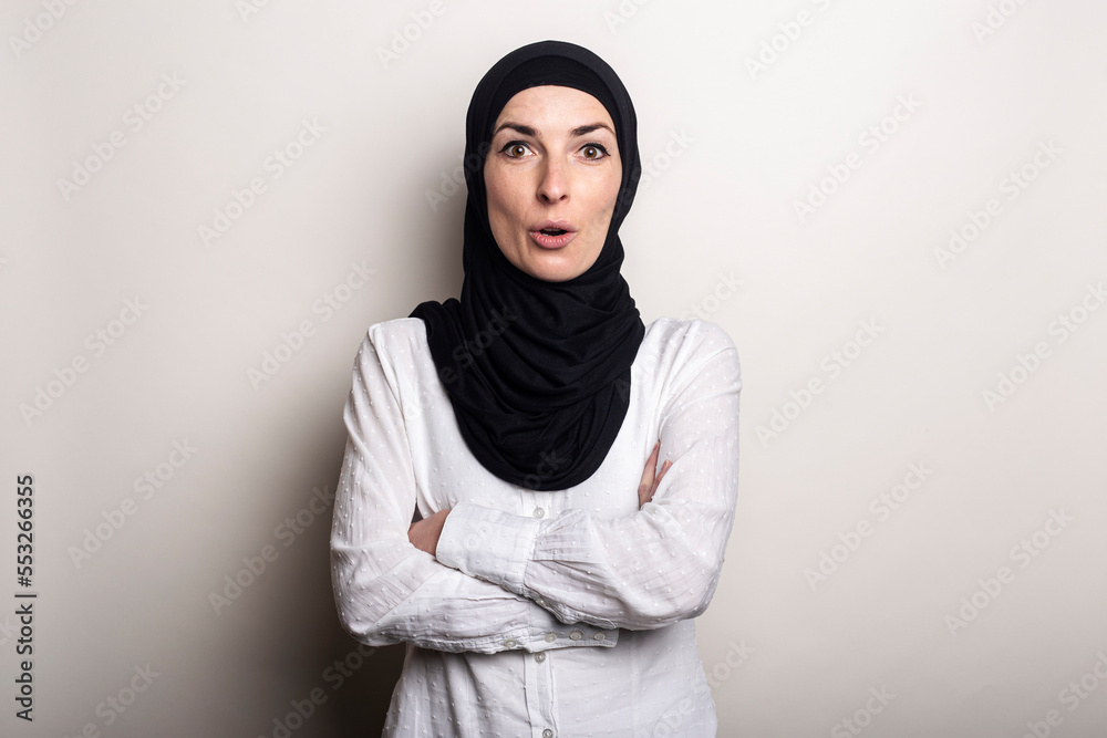 Young woman with surprised face in white shirt and hijab on light background Young woman with surprised face in white shirt and hijab on light background