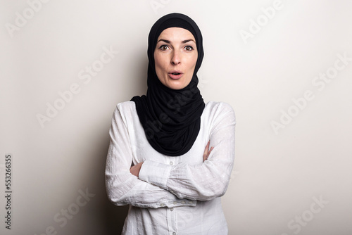 Young woman with surprised face in white shirt and hijab on light background