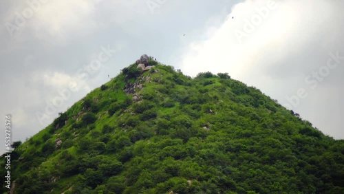 Aravalli range in jaipur rajasthan with birds circling the peak with small hills mountains covered in green trees under monsoon clouds photo