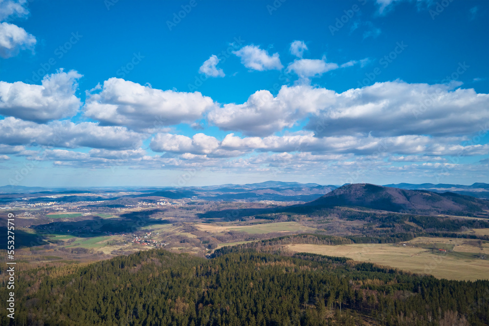 Clouds in blue sky with shadows on ground. A birds eye view of beautiful mountains covered with evergreen forest on sunny autumn day. Natural landscape with mountain ranges and valleys