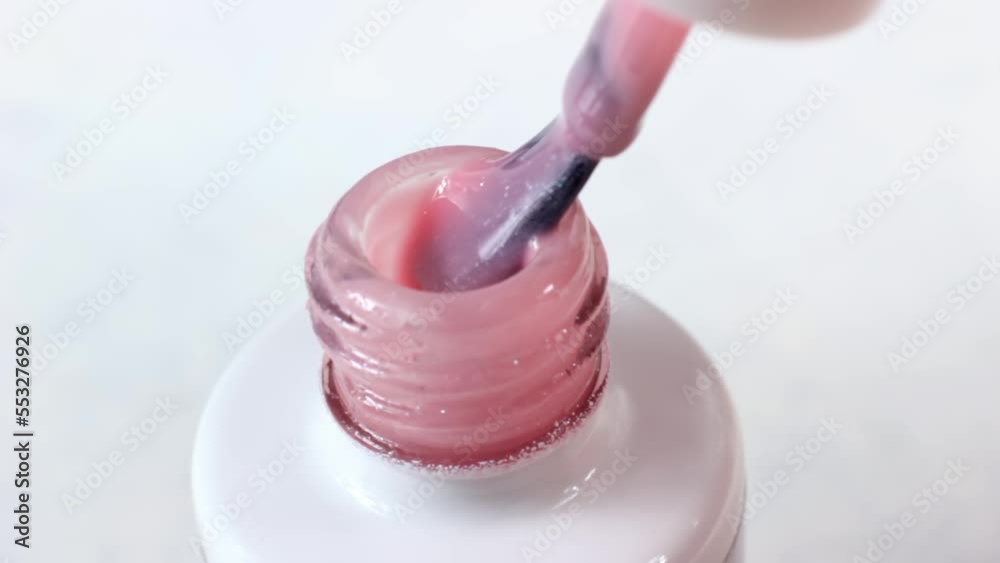 Pastel pink shelak gel nail polish pouring from a brush into the bottle on light background close up Pastel pink shelak gel nail polish pouring from a brush into the bottle on light background close up