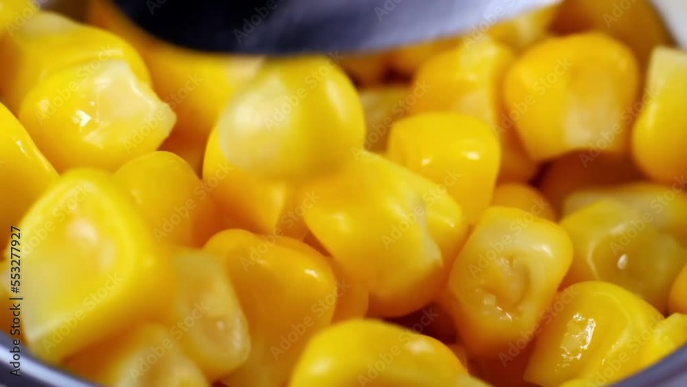 Spoon holding marinated sweet yellow corn seeds in metal can container close up Spoon holding marinated sweet yellow corn seeds in metal can container close up