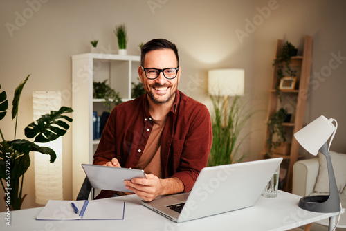 Young man works from home at a desk with a tablet and a laptop