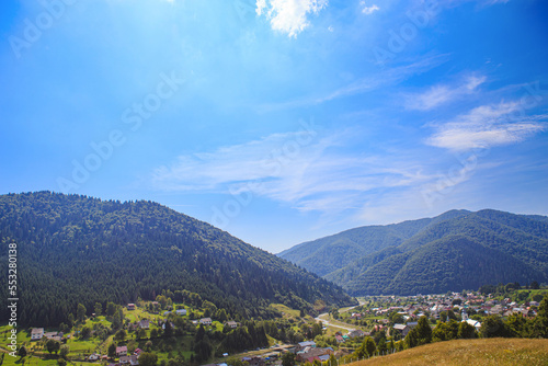The mountains are covered with forests in the lowlands of the mountains village. Rural mountainous area on a sunny day with clouds.