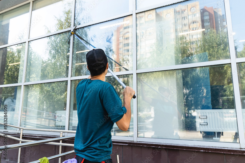 An employee of a professional cleaning service in overalls washes the facade and windows with special devices An employee of a professional cleaning service in overalls washes the facade and windows with special devices