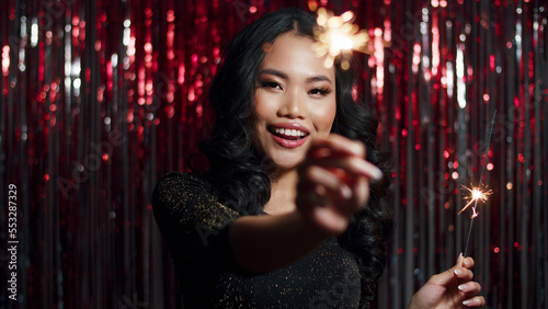 Beautiful asian girl posing with sparkles over red shiny background. 