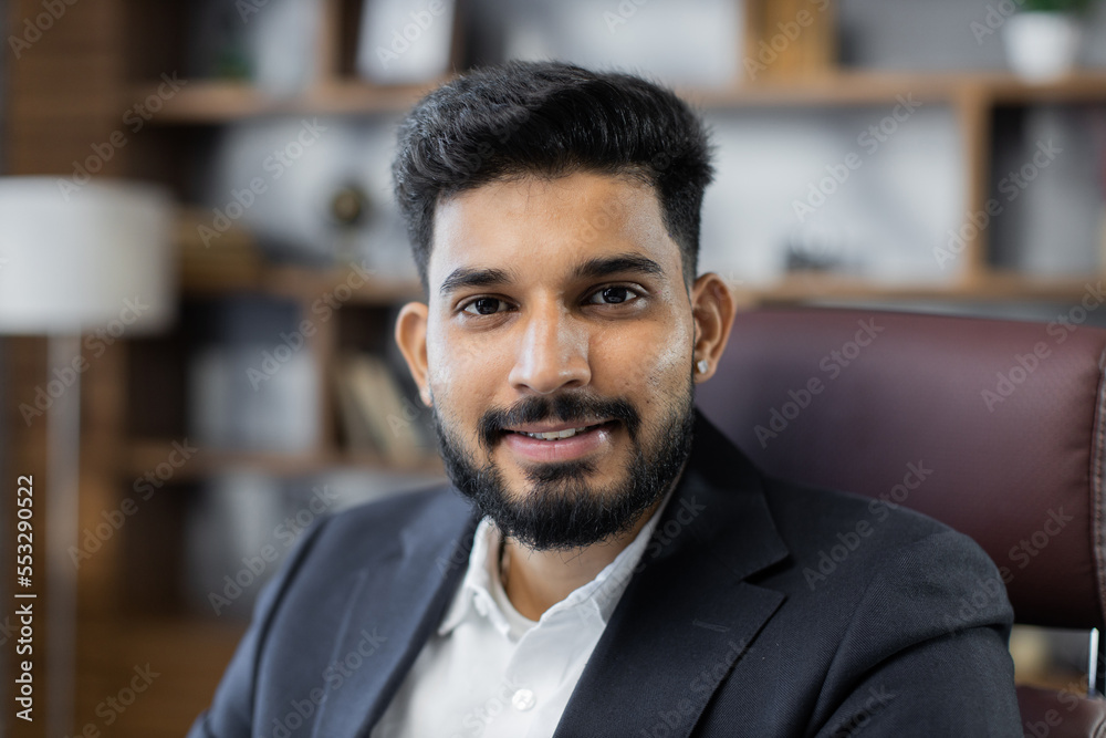 Obraz premium Close up portrait of bearded handsome successful middle east smiling businessman sitting at chair, working in his modern office.