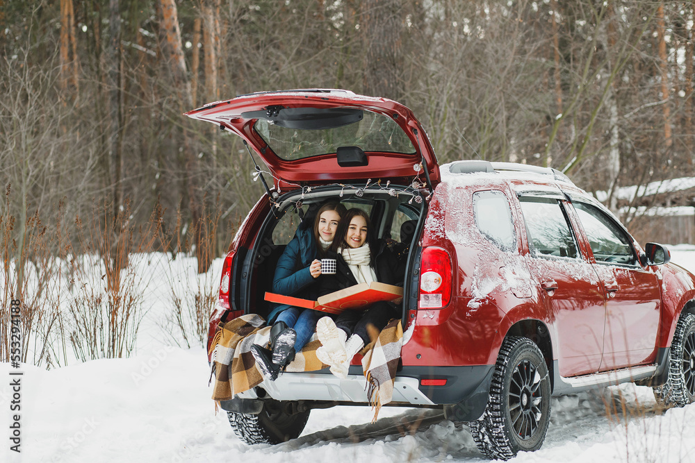 The girls had a picnic in the trunk of a car in the winter forest.
